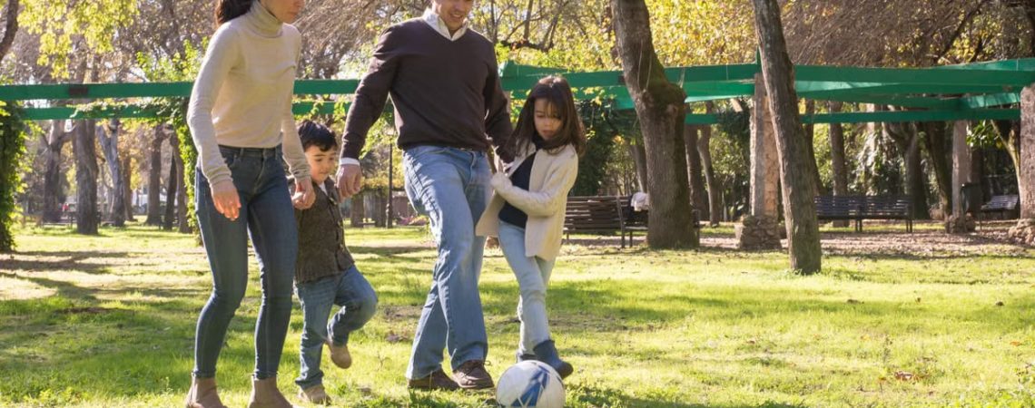 A family plays soccer together in a sunny park, enjoying quality time outdoors.